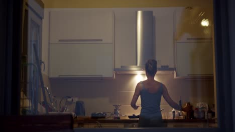 Rear-view-of-a-woman-cooking-in-the-kitchen-at-night