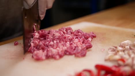 Hand-with-Glove-Chopping-Raw-Beef-with-Pad-Kra-Paw-Ingredient-on-White-Chopping-Board,-Close-Up-1