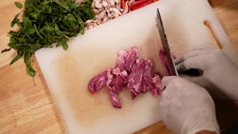 Hand-with-Glove-Use-Knife-to-Slice-Beef-into-Pieces-on-White-Chopping-Board,-Close-Up-1