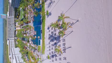 Tiro-Vertical-De-Hotel-Y-Resort-Frente-A-La-Playa,-Paraíso-Tropical-Y-Playa-De-Arena-Blanca-En-Verano-En-Punta-Cana,-República-Dominicana