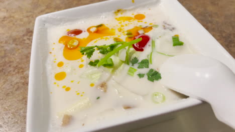 Delicious-Tom-Kha-Gai-Thai-Soup-in-a-white-bowl-with-spoon,-dolly-shot