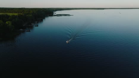 Orbiting-drone-shot-of-a-pontoon-with-a-small-wake-on-a-lake-at-sunset