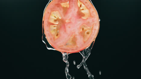 Wasser-Fließt-Frische-Tomatenscheibe-Mit-Flüssigkeitstropfen-In-Zeitlupe-Mit-Hintergrundbeleuchtung-Auf-Schwarzem-Hintergrund