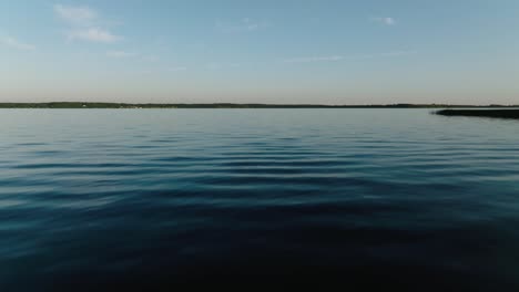 Push-in-aerial-drone-shot-directly-over-a-large-lake-at-sunset