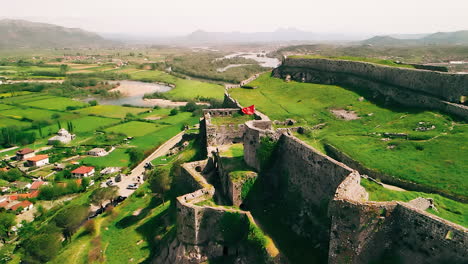 Aerial-view-flying-away-from-the-Albanian-flag-on-castle-ruins-on-a-hill