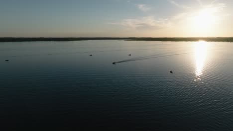 Aerial-drone-shot-of-boats-on-a-large-lake-with-the-sun-setting-in-the-background