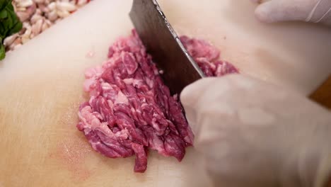Hand-with-Glove-Use-Knife-to-Slice-Beef-into-Pieces-on-White-Chopping-Board,-Close-Up