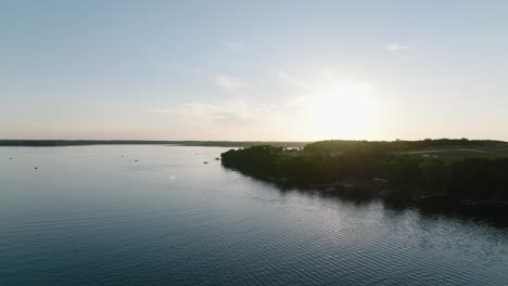 Aerial-drone-shot-of-lake-with-boats-and-the-sun-peaking-over-the-forest-horizon