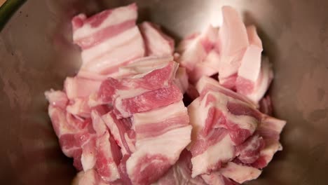 Adding-Raw-Pork-Belly-into-Metal-Mixing-Bowl,-Close-Up