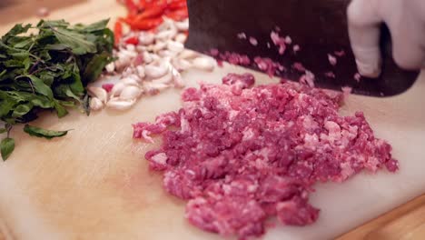 Hand-with-Glove-Chopping-Raw-Beef-with-Pad-Kra-Paw-Ingredient-on-White-Chopping-Board,-Close-Up