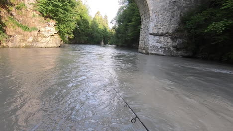 A-fisherman-reels-on-a-big-river-with-strong-current-in-the-Swiss-alps,-fishing-trout