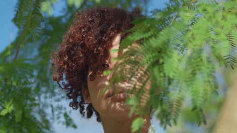 Light-skin-red-hair-girl-facial-close-up-with-leaves-in-the-foreground-on-a-sunny-day-in-the-park