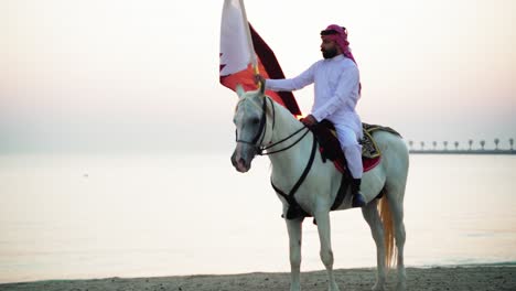 Ein-Ritter-Zu-Pferd,-Der-Die-Katar-flagge-Nahe-Dem-Meer-Hält-9