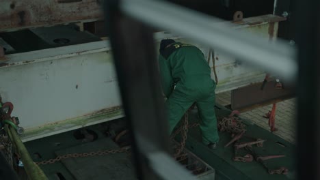 Man-in-green-boiler-suit-moving-heavy-chain-in-preparation-for-lifting-operation