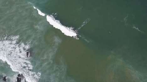 Eine-Drohne-Dreht-Sich-Um-Eine-Luftaufnahme-Von-Surfenden-Surfern-Und-Brechenden-Wellen