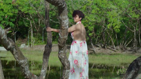 A-hispanic-woman-walking-between-tree-branches-at-the-park-in-a-long-flowing-flower-dress