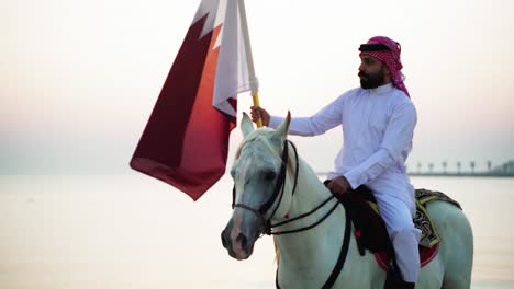 Ein-Ritter-Zu-Pferd,-Der-Die-Katar-flagge-Nahe-Dem-Meer-Hält-6