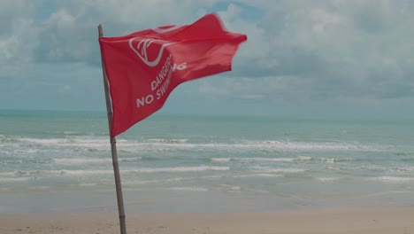 Close-up-warning-flag-at-beach,-Red-flag-sways-in-the-wind,-No-Swiming-zone,-Seascape-Horizon