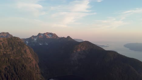 Sunset-Aerial-Drone-Panning-Shot-über-Schneebedeckte-Bergfelsenlandschaft-Mit-Blauem-Und-Orangefarbenem-Himmel-In-Pacific-Ranges-Canada-BC-4k