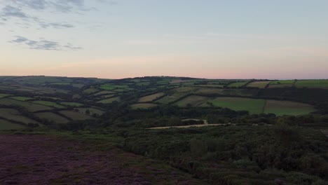 4K-Aerial-Drone-Sunrise-Pushing-Shot-of-Fields-and-Purple-Heather-with-Orange-Lit-Horizon-Exmoor-Devon-UK