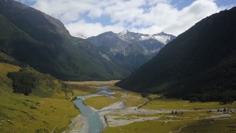 A-forward-aerial-view-over-a-river-in-a-deep-valley-in-New-Zealand-heading-towards-snow-peaked-mountains