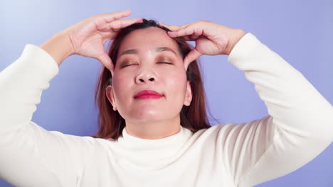 Frustrated-stressed-young-Asian-woman-coping-with-headache-migraine-concept-by-self-head-massage-standing-isolated-over-a-violet-background
