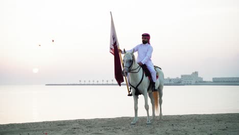 Ein-Ritter,-Der-Auf-Einem-Pferd-Reitet,-Das-Die-Katar-flagge-Nahe-Dem-Meer-Hält-1