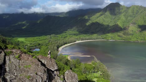 Pareja-Loca-Coqueteando-De-Pie-En-La-Cima-De-Un-Acantilado-Peligroso-En-Una-Caminata-De-Leones-Agazapados-Con-Una-Vista-Panorámica-Excepcional-Del-Valle-Y-La-Bahía-De-Kahana,-Hawaii