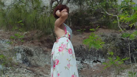 Low-angle-of-a-red-hair-curly-latina-standing-at-rock-cliff-in-a-tropical-Caribbean-park-on-a-sunny-day