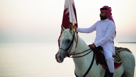 Ein-Ritter-Zu-Pferd,-Der-Die-Katar-flagge-Nahe-Dem-Meer-Hält
