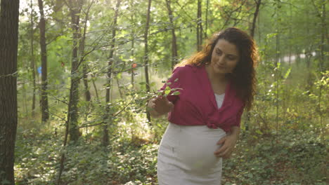 Closeup-pregnant-mom-walking-thru-forest-brushing-tree-branch-and-holding-belly