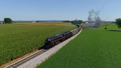 An-Aerial-View-of-an-Antique-Steam-Passenger-Train-Approaching-After-Going-around-a-Curve-Blowing-Smoke-and-Steam-Traveling-Thru-Fertile-Corn-Fields-During-the-Golden-Hour-on-a-Sunny-Summer-Day