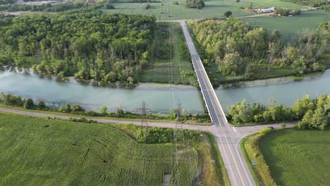Power-lines-from-grid-over-river-water-in-rural-countryside-aerial-tilt-down