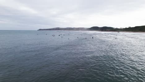 Aerial-drone-shot-of-dozens-of-surfers-swimming-over-big-waves-at-Playa-Meron-Beach-in-San-Vicente-de-la-Barquera