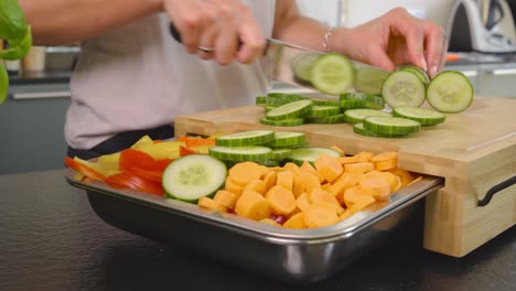 Low-panning-shot-of-a-women-cutting-cucumber-while-preparing-a-bowl-of-fresh-veggies-in-a-clean-modern-kitchen