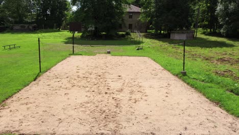 Slow-passing-aerial-view-across-empty-sand-volleyball-court-in-Latvian-countryside-grassy-garden