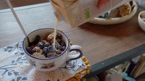 Plant-based-milk-poured-over-a-bowl-of-healthy-cereals-with-frozen-berries-in-4K-slow-motion