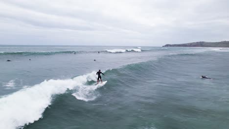 Aerial-drone-shot-of-surfers-riding-high-waves-at-Playa-Meron-Beach-in-San-Vicente-de-la-Barquera