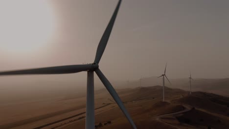 Close-up-tracking-aerial-shot-of-a-wind-turbine-at-sunset-or-sunrise-on-a-dusty-foggy-day