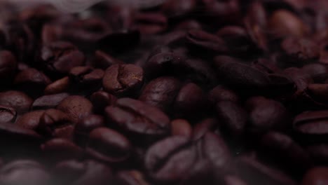 Zooming-in-close-up-shot-of-roasted-coffee-beans-with-smoke-wafting-down-onto-them