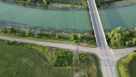 Electricity-Power-lines-above-river-water-in-rural-countryside-aerial-tilt-down