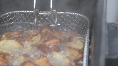 Potato-wedges-frying-in-fryer-with-boiling-hot-oil,-steam-rising,-close-up