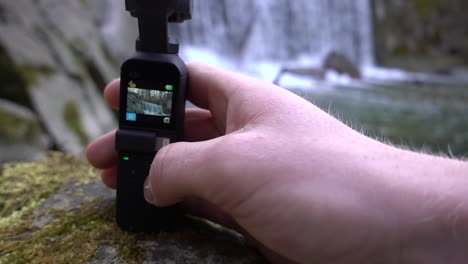 A-filmmaker-is-setting-its-dji-osmo-pocket-camera-next-to-a-small-swiss-alps-river