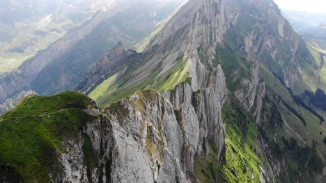 Aerial-flyover-over-the-cliffs-of-Schafler-ridge-in-Appenzell,-Switzerland-with-pan-up-towards-the-mountains-including-Altenalpturm
