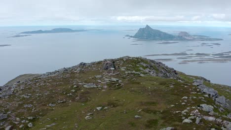 Hiker-On-Top-Of-A-Rocky-Mountain-Overlooking-Scenic-Islands-And-Fjords-In-Norway---aerial-orbit