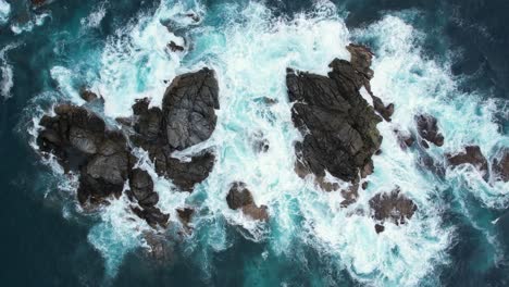 Aerial-Footage-of-the-ocean-waves-hitting-a-group-of-rocks-near-playa-del-muerto-in-Mazunte,-Oaxaca-in-slow-motion
