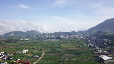 Aerial-flyover-Dieng-Regency-in-Central-Java-with-rural-plantation-fields-and-village-houses-surrounded-by-mountains-during-sunny-day-in-Indonesia