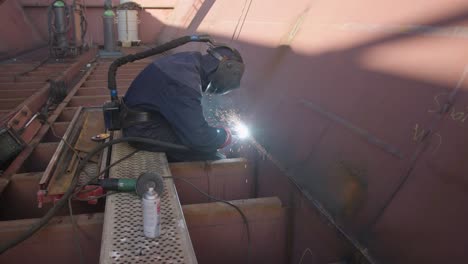 Close-up-of-professional-worker-welding-inside-large-metal-container,-side-view