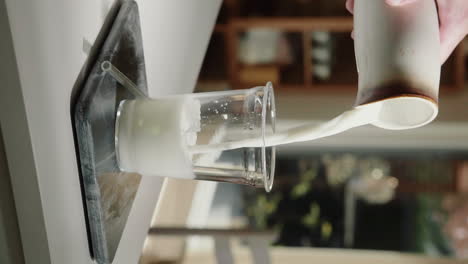 Vertical-Video-pouring-vegan-milk-on-ice-into-glass-cup-with-glass-straw-in-slow-motion-close-up