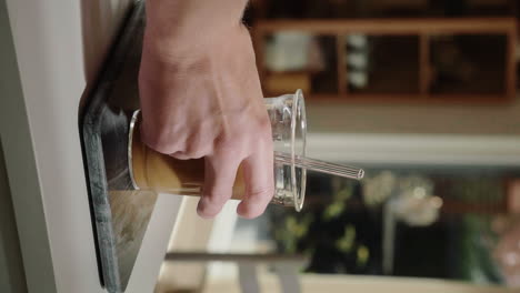 Vertical-Video-hand-grabbing-refreshing-iced-latte-from-the-kitchen-counter-in-slow-motion-close-up-homemade-cold-brew